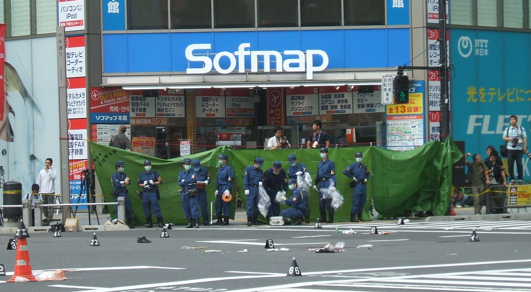 Intersection where the suspect's truck struck pedestrians in the so-called Akihabara Massacre. Pictured are inspectors surveying the scene, as well as blood-stained towels and personal items (thought to belong to the victims) scattered on the street.