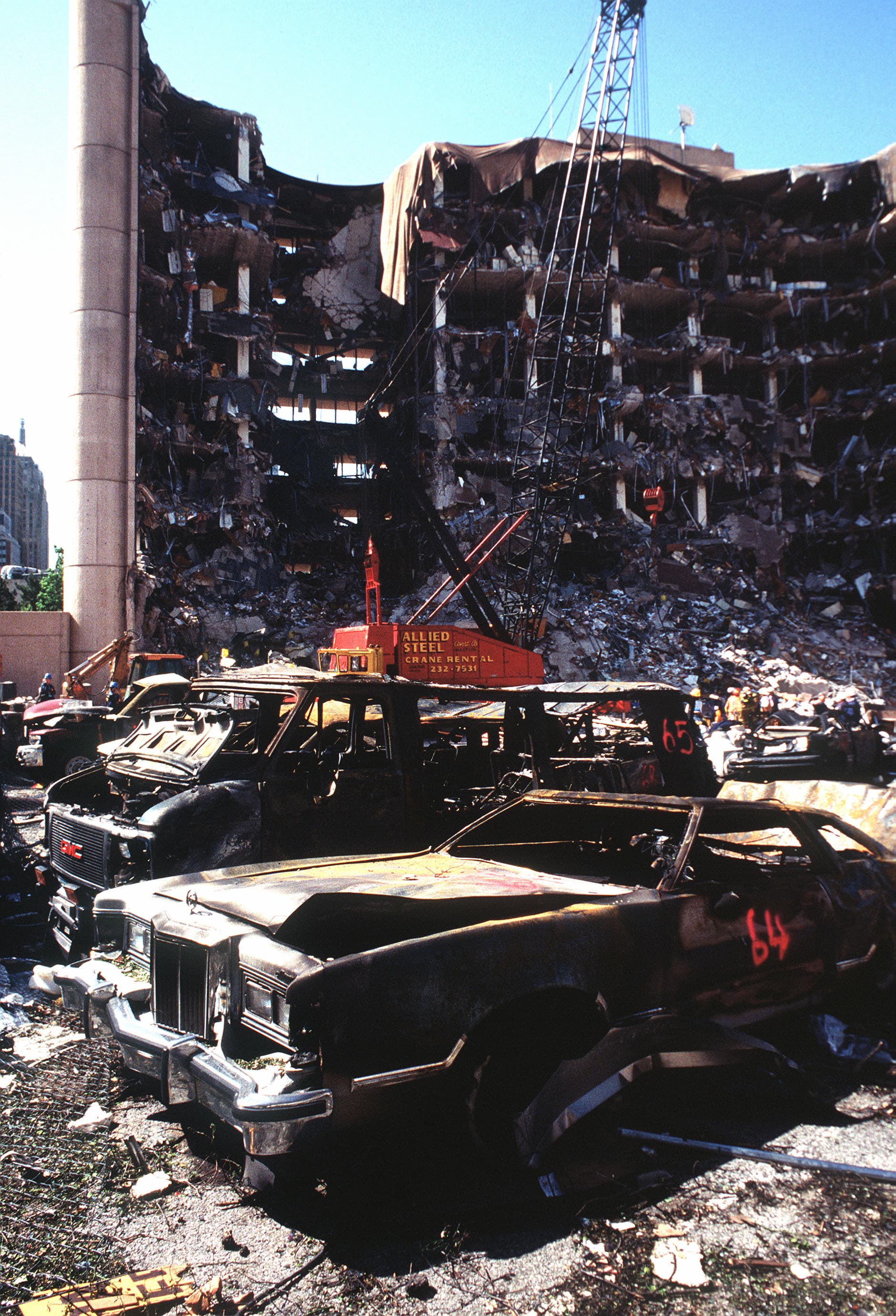 The bombed remains of automobiles with the bombed Federal Building in the background. The military is providing around the clock support since a car bomb exploded inside the building on Wednesday, April 19, 1995.